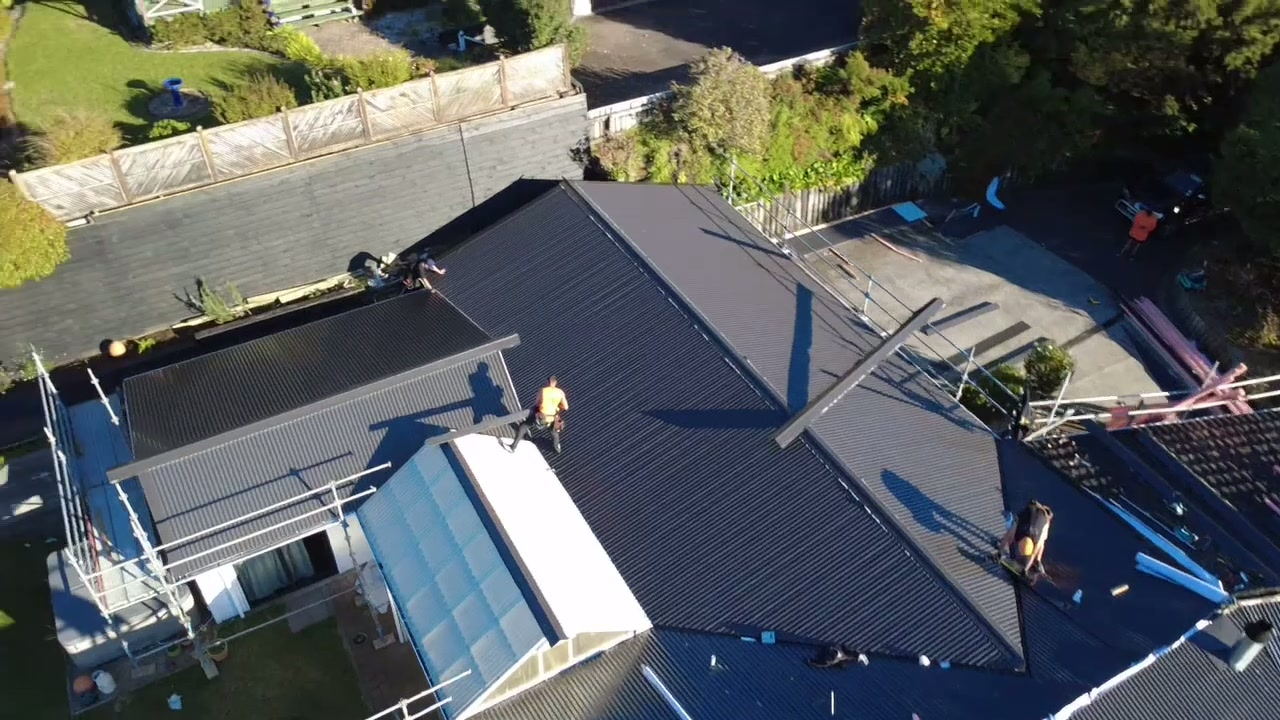 Roofer working at the ridge of a partly re-roofed house, with the scaffold around it