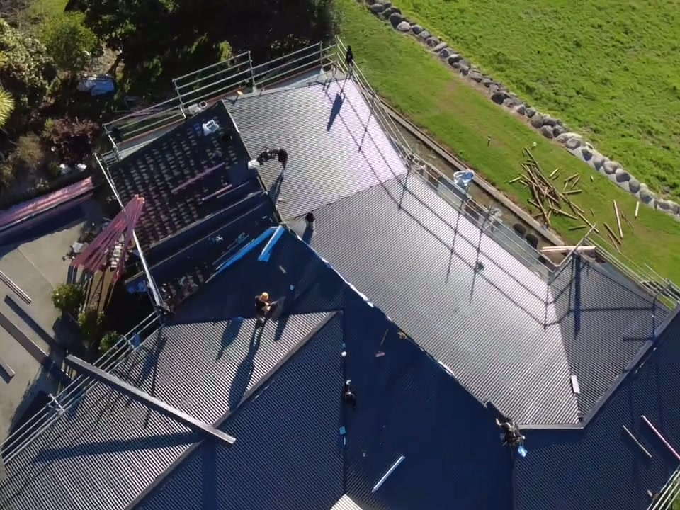 Two roofers laying new sheets on a hip roof, seen from above