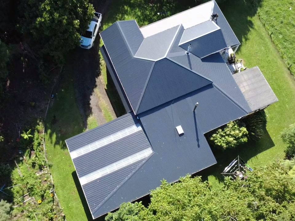 Aerial view of a finished dark longrun roof on a Taranaki home surrounded by lawn and bush