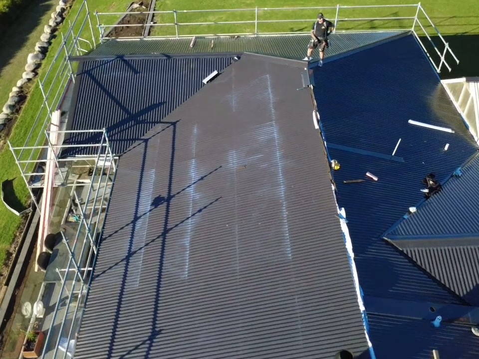 Roofer working along a long run of new corrugate with the scaffold rail in front