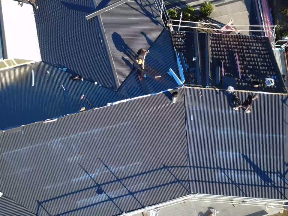 New dark roofing sheets laid across most of a Taranaki house, with a roofer at the ridge
