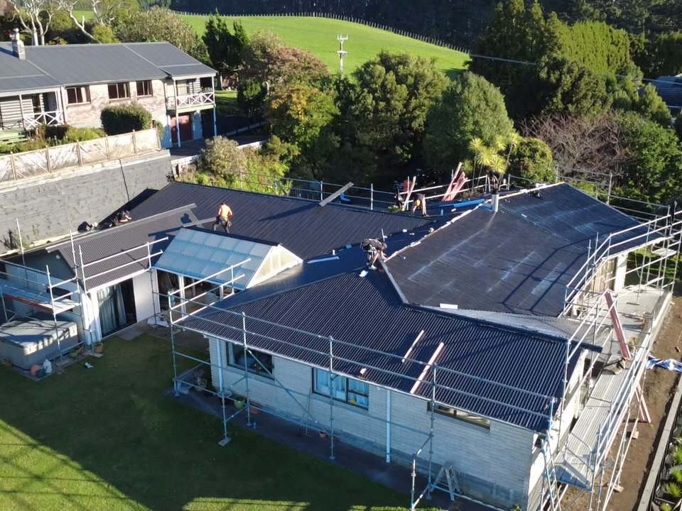 Wide aerial view of a house under scaffold part way through its re-roof, with the neighbouring properties behind