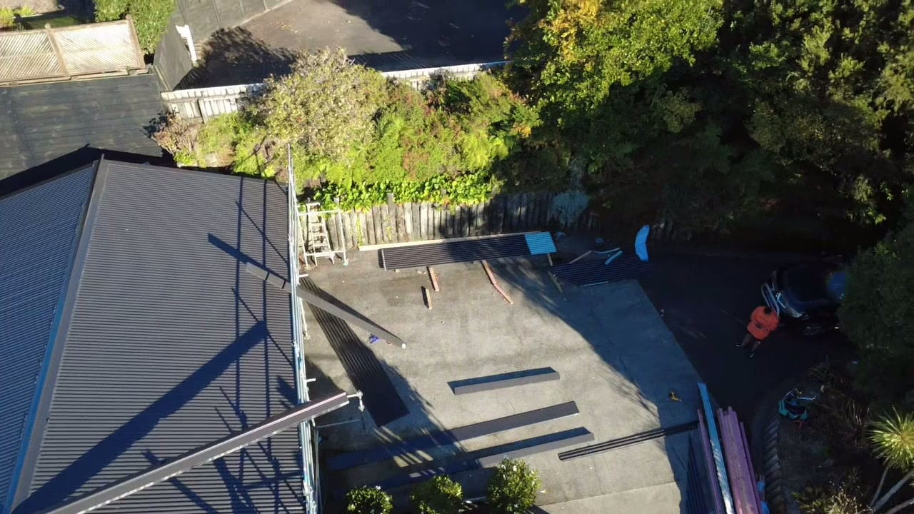 Overhead view of a freshly roofed dark hip roof with the scaffold still up along the edge