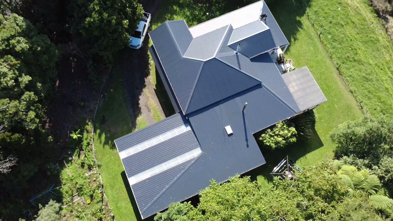 Aerial view of a finished dark grey longrun roof on a Taranaki home surrounded by lawn and native bush