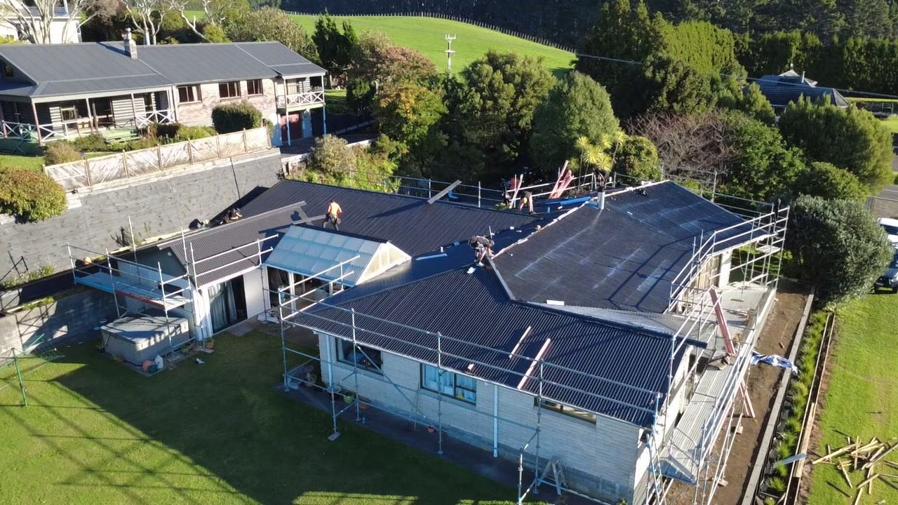 Aerial view of a Taranaki house under scaffold part way through a re-roof, with new dark sheets on the main roof