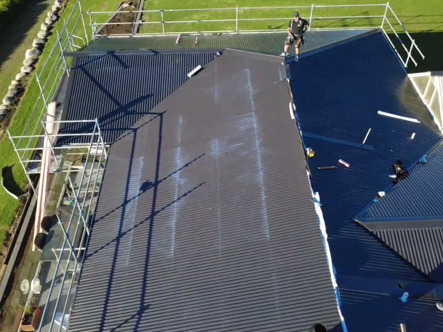 Roofer fixing a long run of new dark corrugate roofing